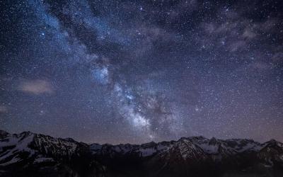 The night sky full of stars and the milky way galaxy diagonally crossing above a mountainous horizon. 