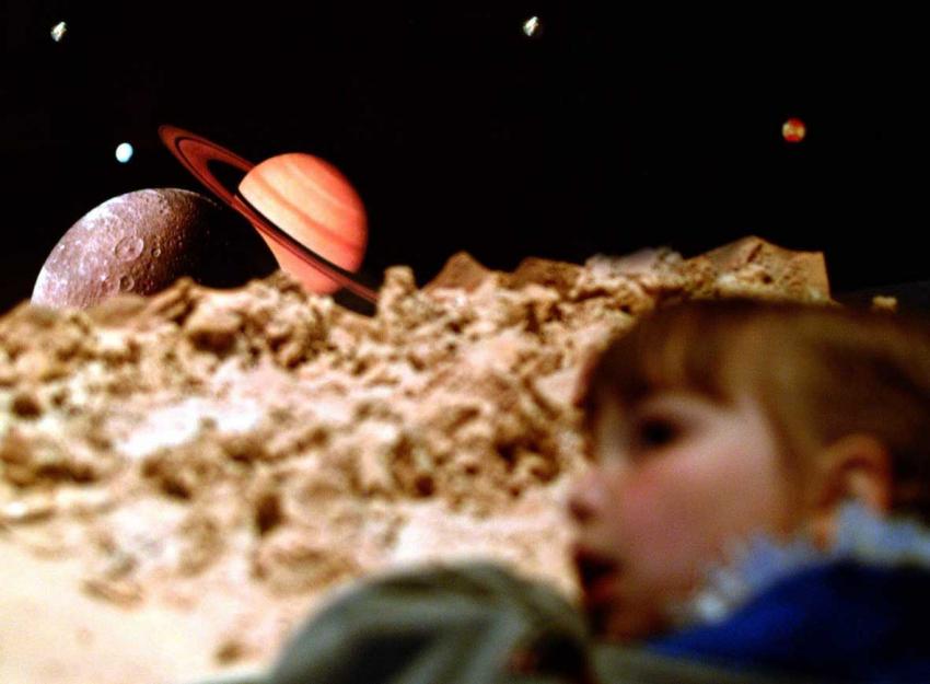 A young girl inside a planetarium in awe of the view if the solar system.