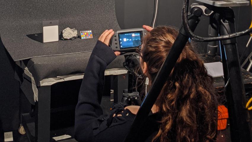 A person photographing a small piece of meteorite surrounded by lab equipment