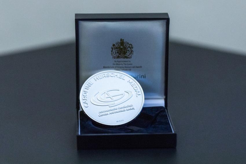 An image of the Caroline Herschel Medal. The medal is silver, and has the German Astronomical Society logo in the centre.