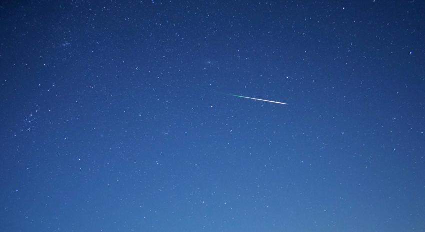 An image of a blue night sky with a single meteor visible in the centre of the frame.