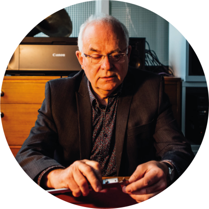 Dark image of a man sitting behind a desk using calipers to measure. 