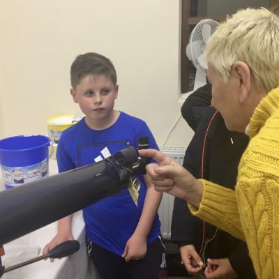 An astronomer showing a child where to look through a telescope; using the eyepiece. 